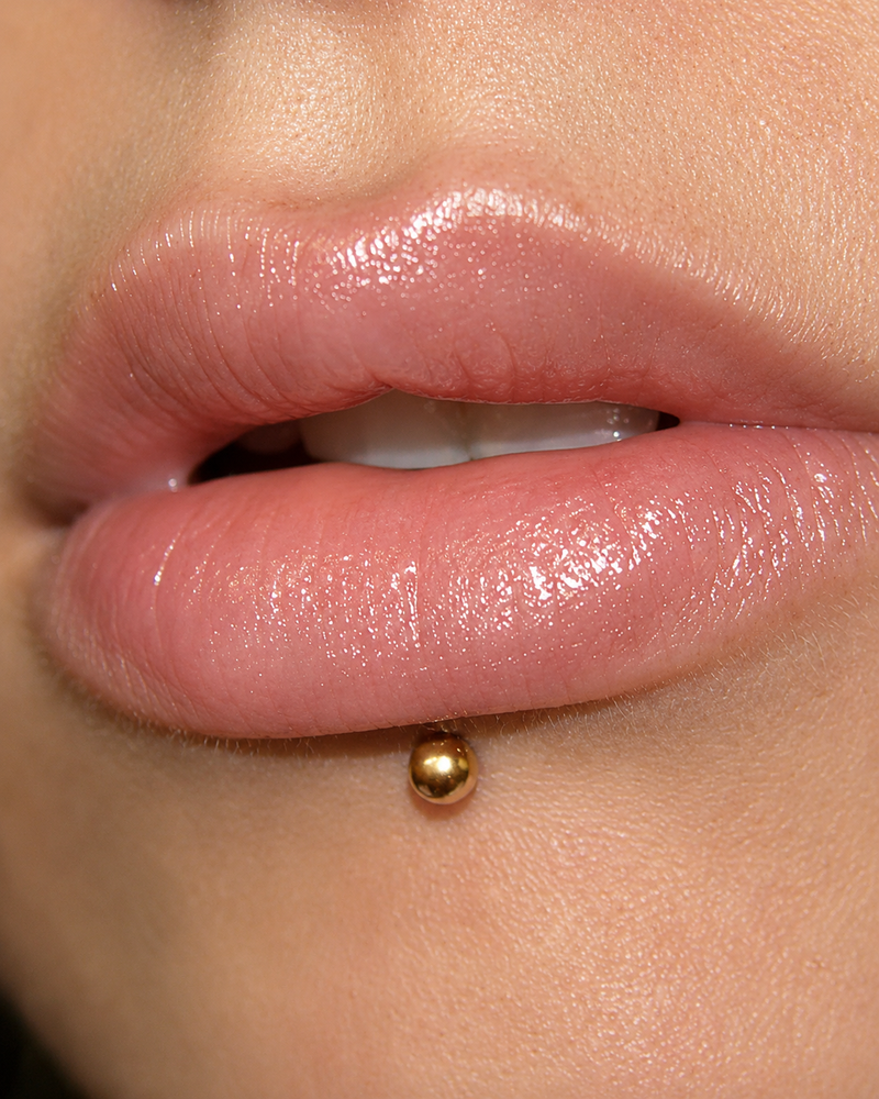 Labret piercing with a gold ball flat back stud, centred below the lower lip