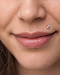 Monroe piercing - 14k yellow gold diamond flat back stud on the upper lip, worn on the wearer's left