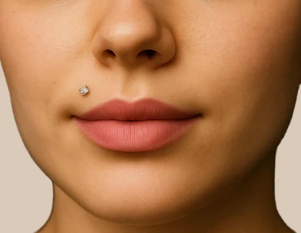 Close-up of a person's face with a diamond stud lip piercing on a beige background