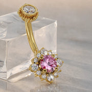 14k yellow gold halo belly ring with pink sapphire center and diamond halo, angled on crystal block