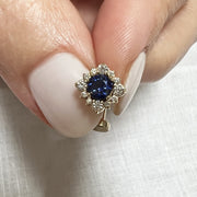 14k yellow gold floating belly ring with blue sapphire center held between fingers for scale