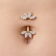 A close-up of a gold belly button ring with marquise-cut clear stones, shown worn on a person's navel.