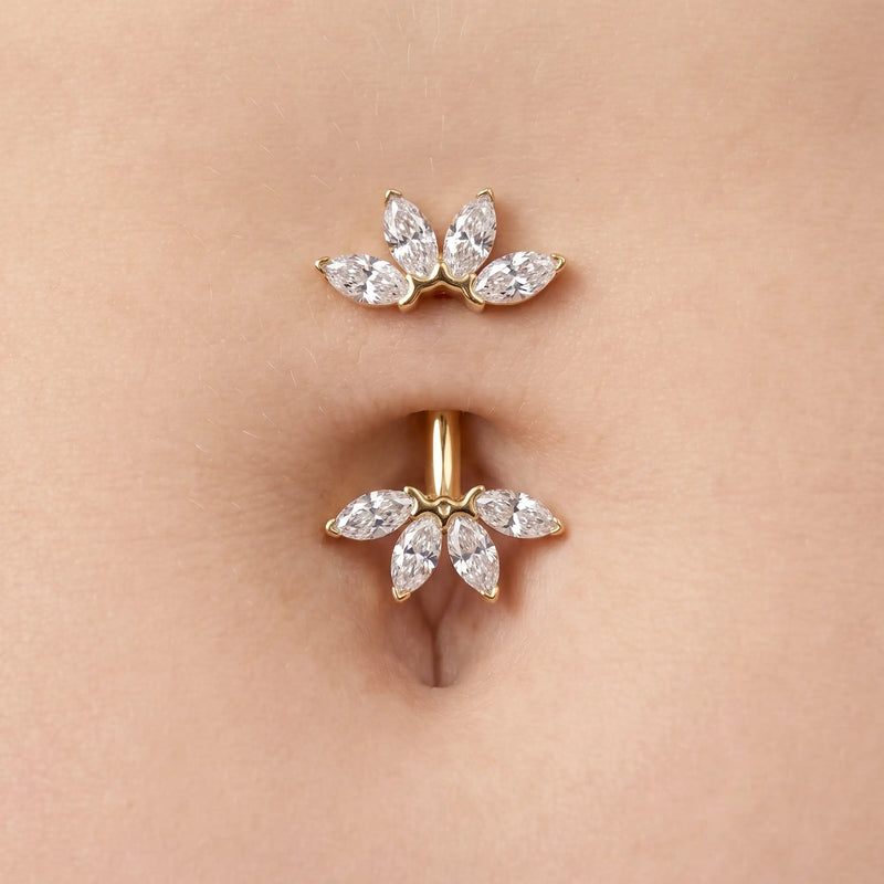 A close-up of a gold belly button ring with marquise-cut clear stones, shown worn on a person's navel.