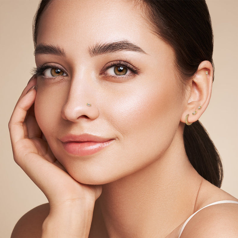 Model wearing 14K yellow gold baguette diamond stud in lobe and helix piercings, lifestyle shot