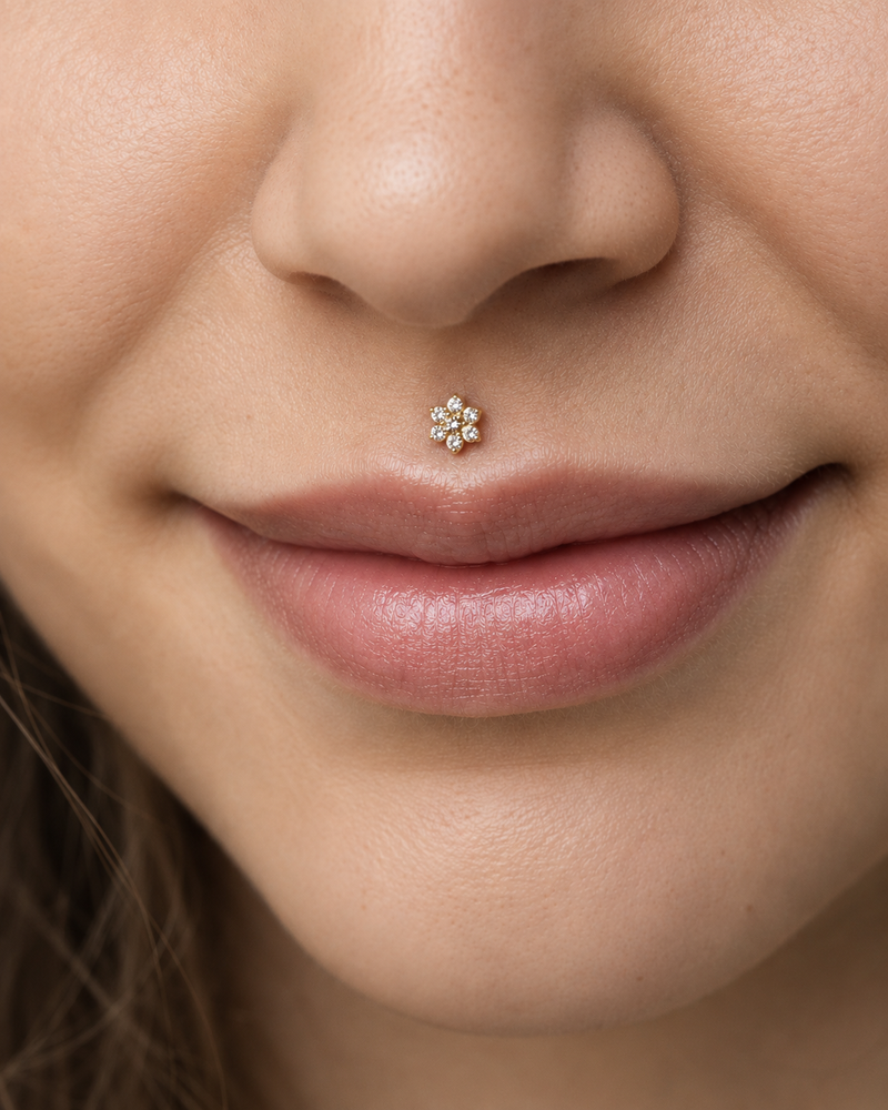 Medusa piercing with a gold flower flat back stud, centred in the philtrum above the upper lip