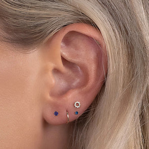 2mm sapphire solitaire stud shown styled in multiple ear piercings on a model with blonde hair