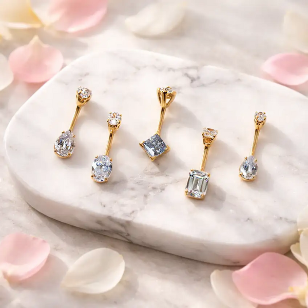 Belly rings with gemstones on a marble surface with pink petals