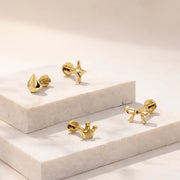 14k yellow gold crown labret stud grouped with star, bow, and droplet flat back studs on marble tile