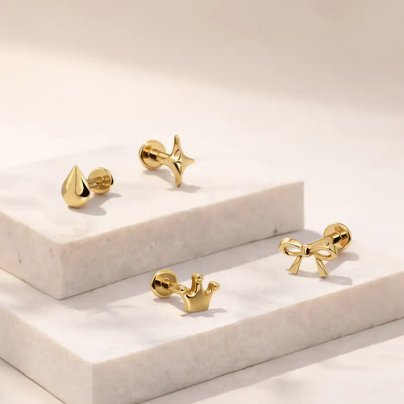 14k yellow gold crown labret stud grouped with star, bow, and droplet flat back studs on marble tile