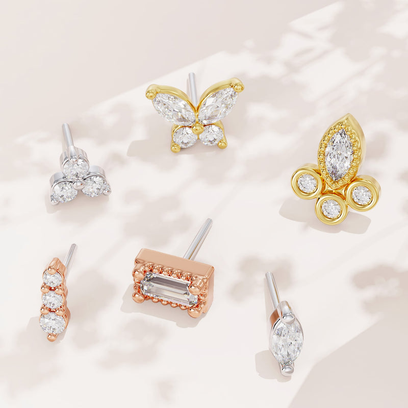 Assorted diamond threadless stud ends in yellow, rose, and white gold displayed on cream surface
