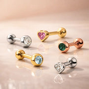 Lifestyle flatlay of assorted 14K gold gemstone tongue and cartilage barbells in yellow, white, and rose gold