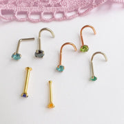 Flat lay of assorted gold nose rings in twist, L-shape, and bone styles with multicolor gemstones