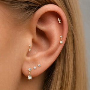 Close-up of an ear wearing multiple gold and diamond earrings against a neutral background