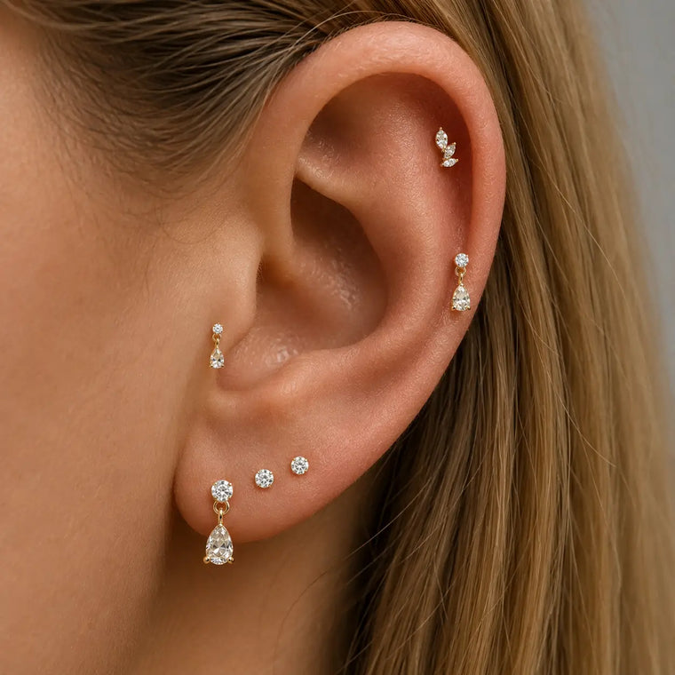 Close-up of an ear wearing multiple gold and diamond earrings against a neutral background