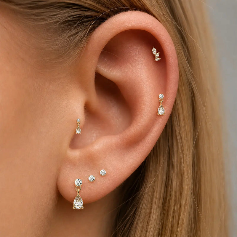 Close-up of an ear wearing multiple gold and diamond earrings against a neutral background