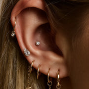 Pear diamond flat back stud worn in outer conch piercing within a curated gold ear stack on model