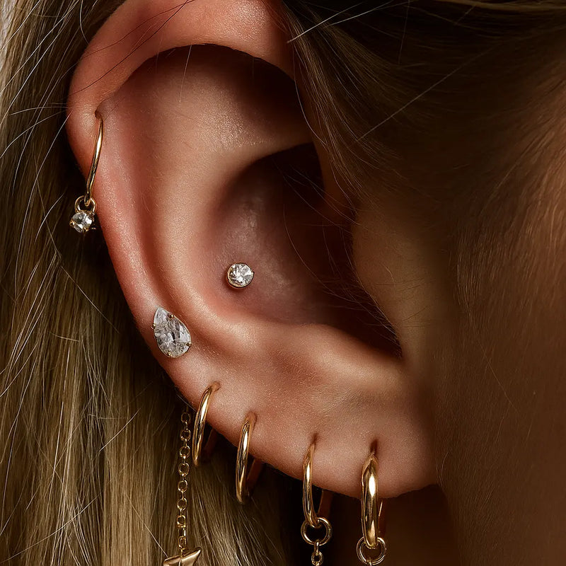 Pear diamond flat back stud worn in outer conch piercing within a curated gold ear stack on model