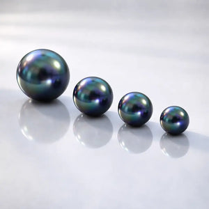 All four peacock pearl bead sizes side by side showing iridescent blue-green luster on reflective surface