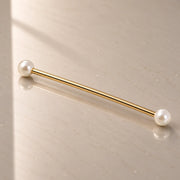 A gold industrial barbell with white pearl ends, resting diagonally on a light gray reflective surface.