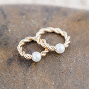 Two 14K yellow gold twisted pearl captive bead rings in different sizes resting on stone surface