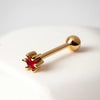 14k yellow gold flower cartilage stud with ruby gemstone, angled lifestyle view on white surface
