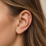 Clear glass piercing retainers worn in a helix piercing and two lobe piercings on a model's ear