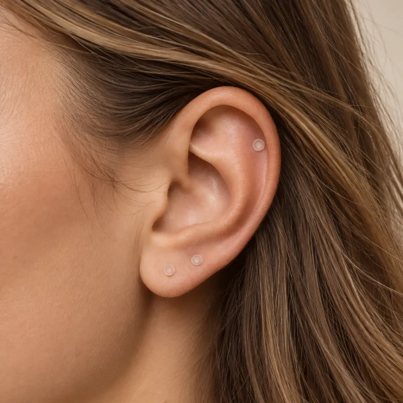 Clear glass piercing retainers worn in a helix piercing and two lobe piercings on a model's ear
