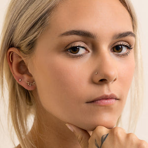 Aries constellation 14k gold flat back earring worn in model's lobe piercing, styled with ear stack