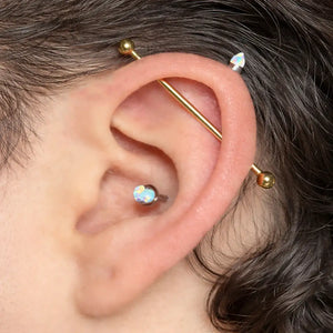 Gold industrial barbell shown in a cartilage piercing on a model's ear for fit and scale reference