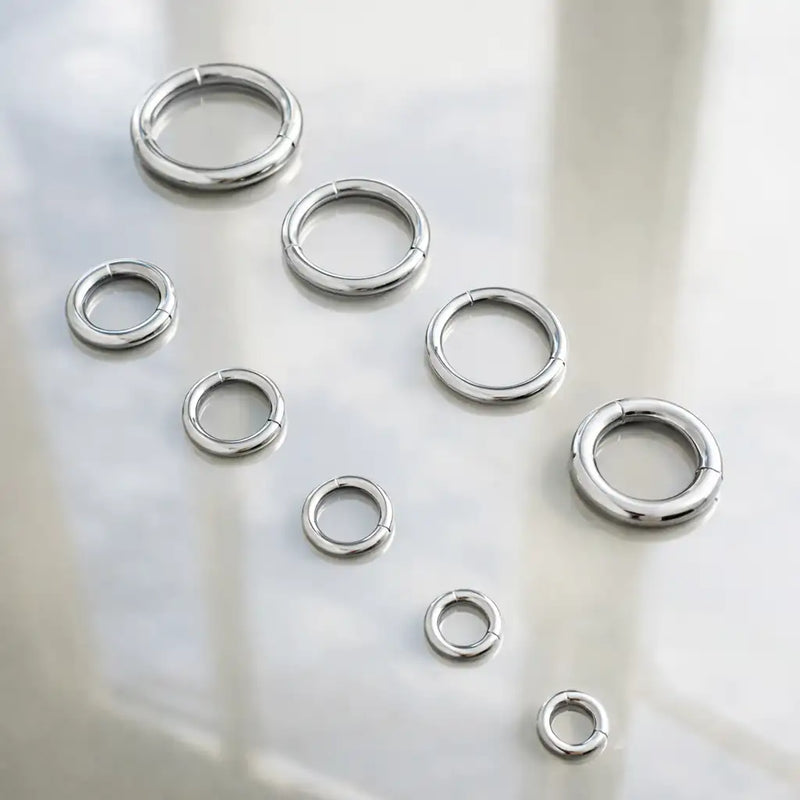18K white gold plain clicker hoops in multiple sizes and gauges scattered on frosted glass surface