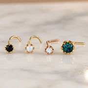 Four Reina nose studs on white marble - black diamond and white opal screws in yellow gold, a diamond L-bend in rose gold and a larger black opal L-bend in yellow gold