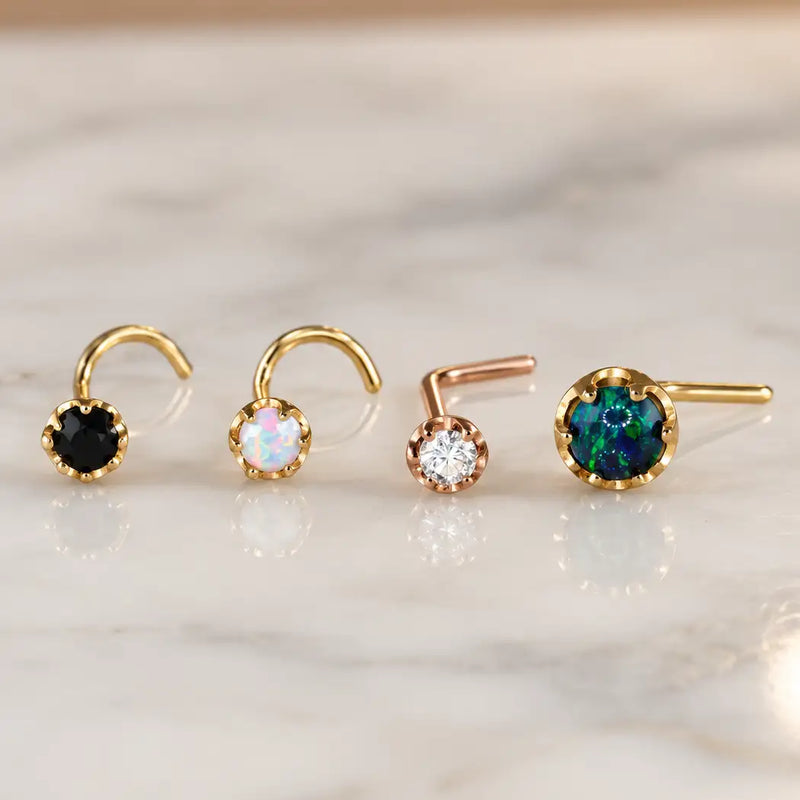 Four Reina nose studs on white marble - black diamond and white opal screws in yellow gold, a diamond L-bend in rose gold and a larger black opal L-bend in yellow gold
