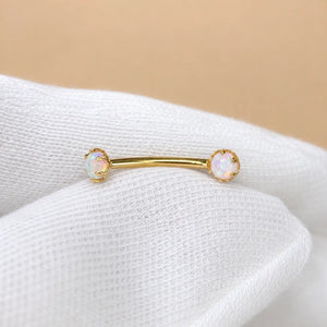 A gold curved barbell with two round white opal gemstones, displayed on a textured white fabric against a warm beige background.