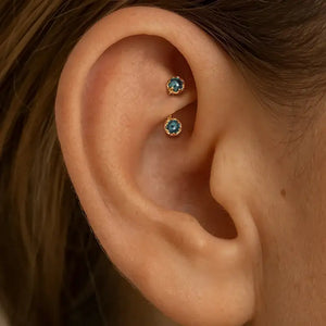 Close-up of an ear wearing the Reina London Blue Topaz curved barbell in a rook piercing.