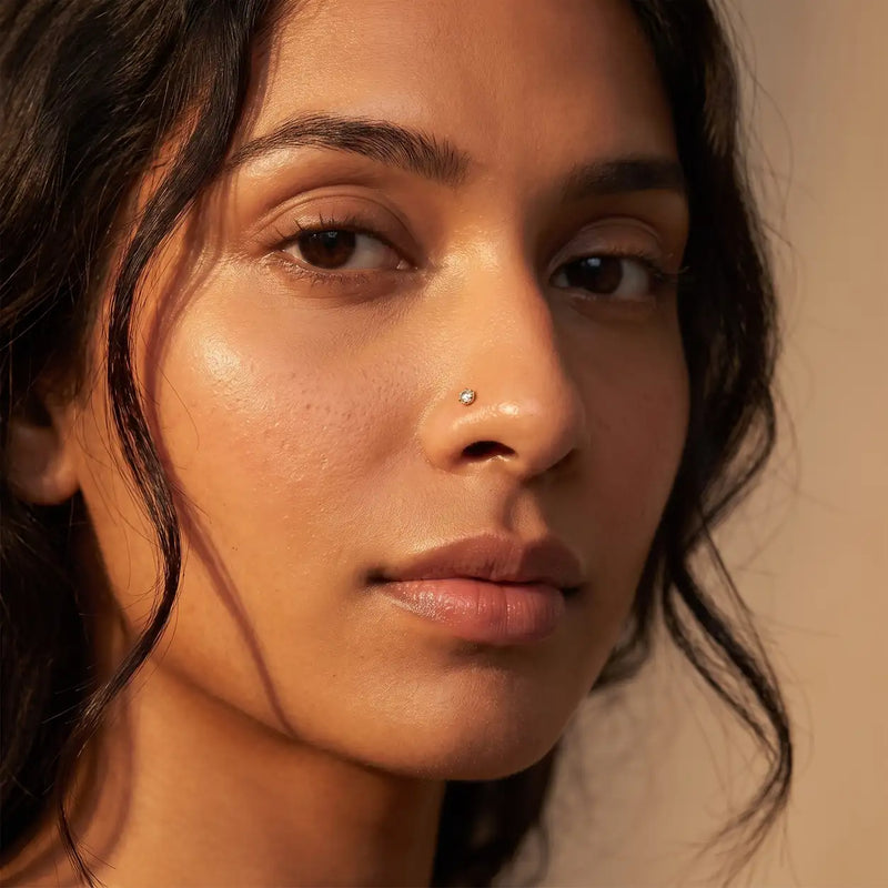 3mm Reina rose cut diamond nose ring in 14k yellow gold worn in a nostril piercing, close-up on a female model