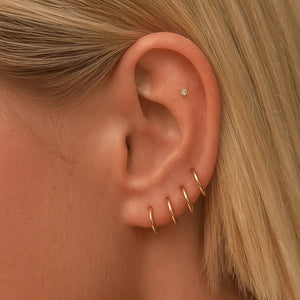 Multiple 18K yellow gold clicker hoops stacked across lobe and cartilage piercings on model's ear