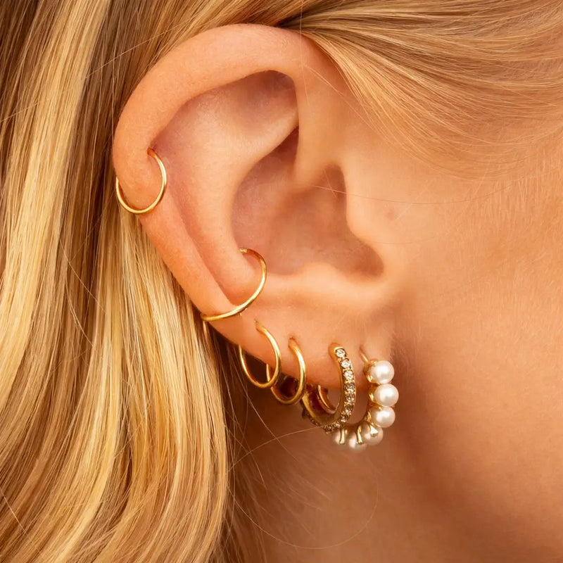 18K yellow gold clicker hoops in graduated sizes styled across helix and lobe piercings, ear stack