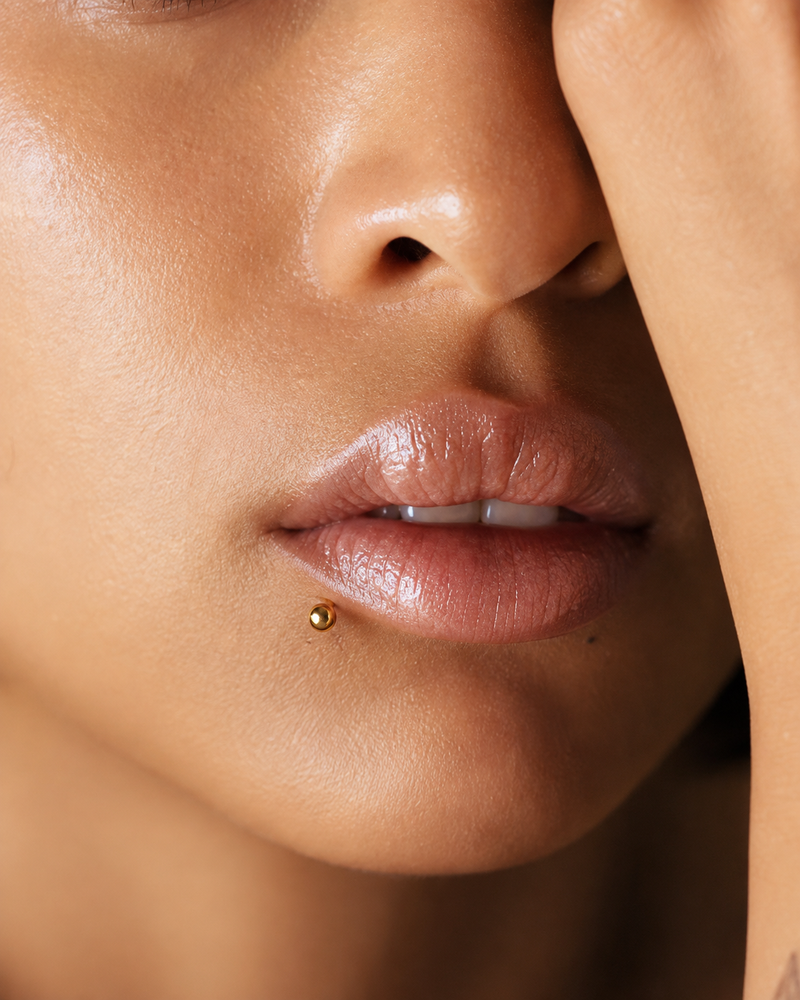 Side labret piercing with a gold ball stud, set off-centre on the lower lip