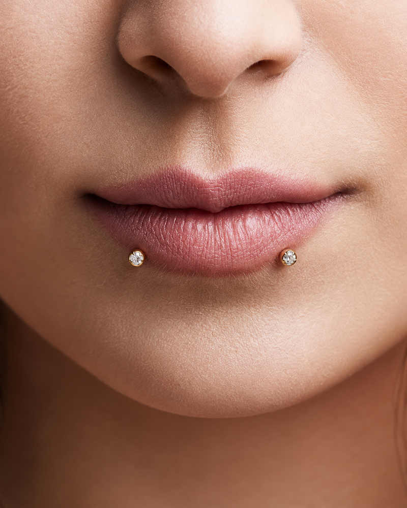 Snake bites piercing with a pair of gold prong-set studs, one either side of the lower lip