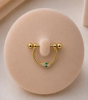 A yellow gold stirrup piercing with snake detailing, displayed on a round beige jewelry stand.