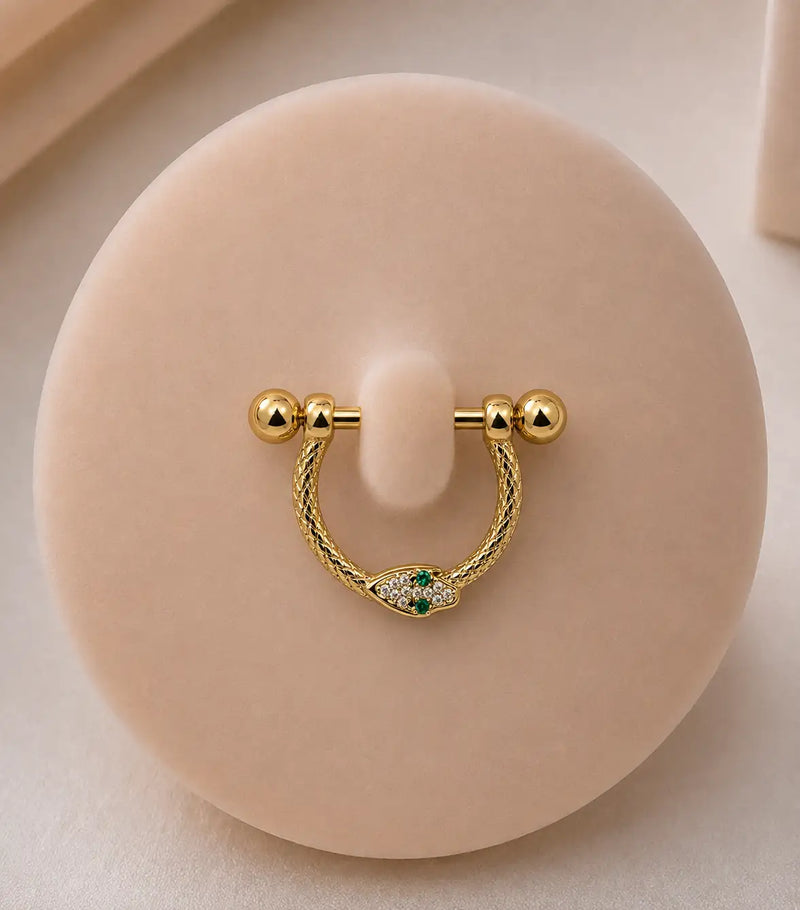 A yellow gold stirrup piercing with snake detailing, displayed on a round beige jewelry stand.