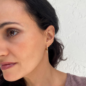 14K gold tiny disc flat back earring worn in helix piercing, styled with multiple gold ear piercings
