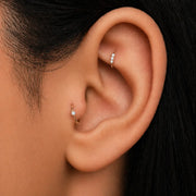 Three-diamond gold seam ring worn in helix piercing, shown alongside a tragus hoop