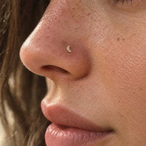 Close-up of a person's nose wearing a small crescent moon stud with a tiny clear gemstone.