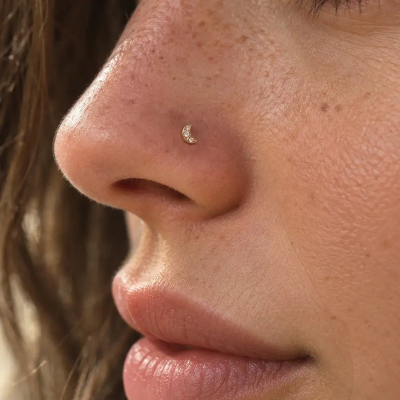 Close-up of a person's nose wearing a small crescent moon stud with a tiny clear gemstone.