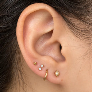 Curated gold ear stack with tiny charm flat back studs shown on a model's lobe and cartilage piercings