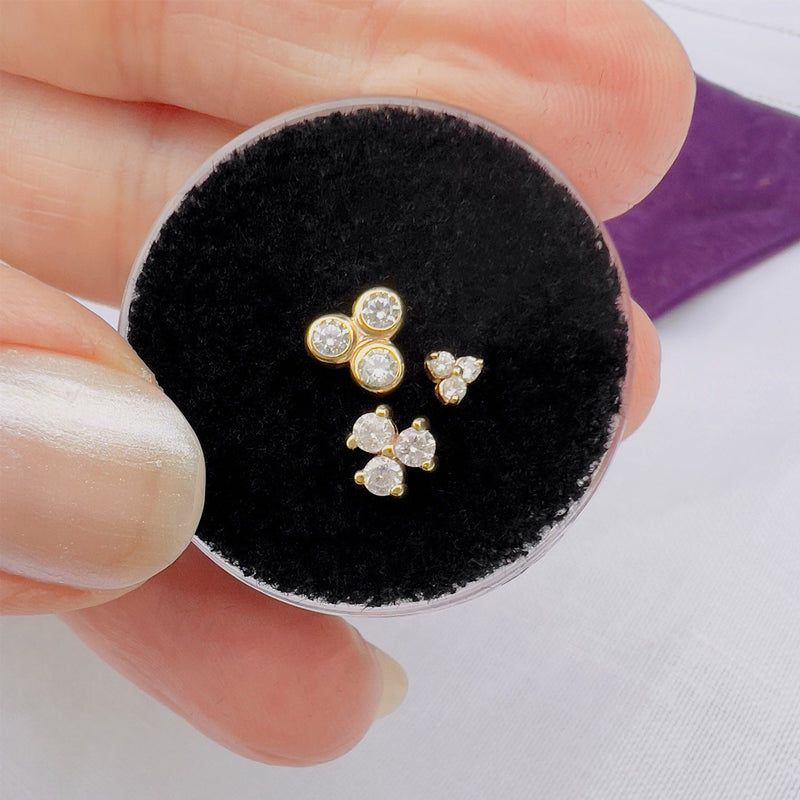 Three gold triple-diamond cluster stud tops held for size comparison in FreshTrends packaging