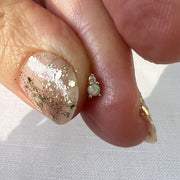 Tiny 14k gold opal and diamond piercing stud end pinched between fingertips, close-up scale view