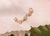 Gold earring with clear gemstones on a soft pink fabric background