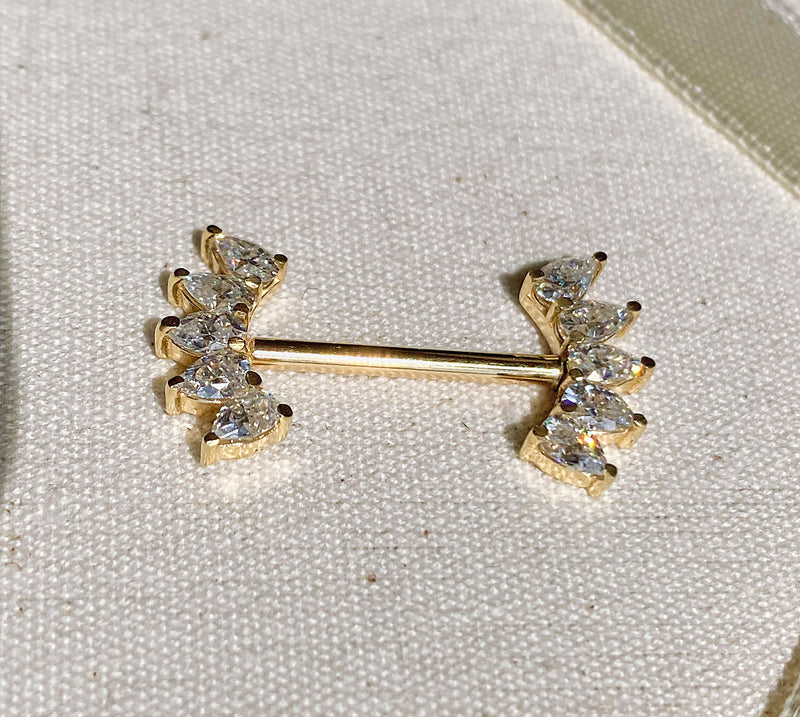 14k yellow gold white sapphire crescent nipple barbell resting on linen fabric, lifestyle shot